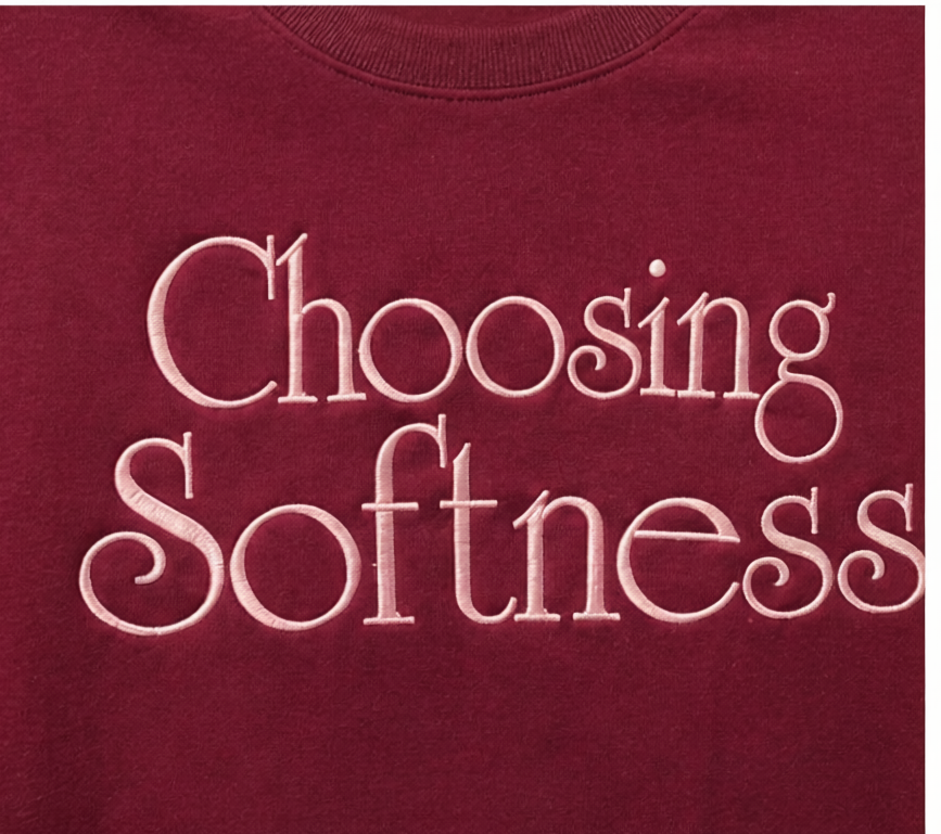 Close-up of light pink Choosing Softness embroidery on burgundy tee